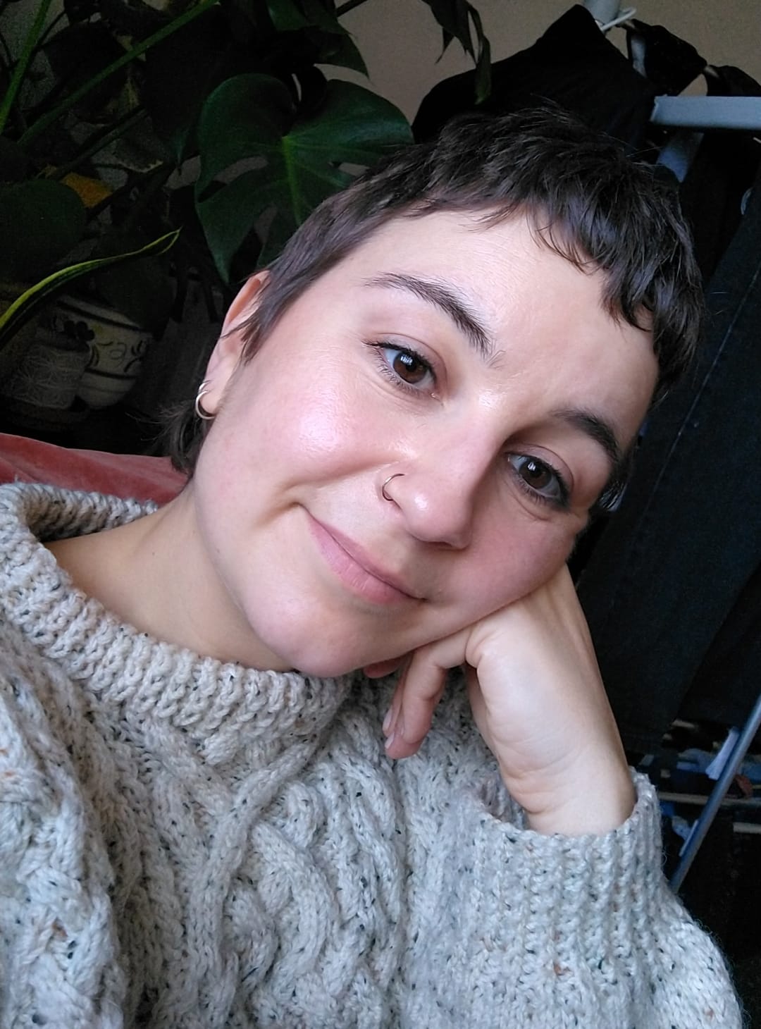 Image of a white woman with cropped brown hair, wearing a cream wool jumper, leaning on her left hand and looking into the camera